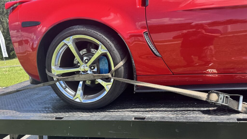 A close-up of a red sports car's wheel securely strapped onto a TP Towing flatbed truck in Tampa, FL.