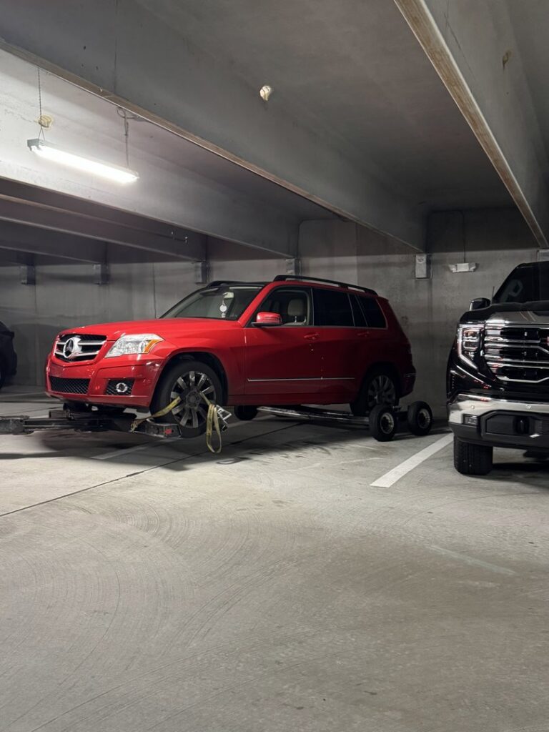 A red SUV being towed by a wheel-lift tow truck from A-Tow Atlanta / Alpharetta in a parking garage in Atlanta, GA.