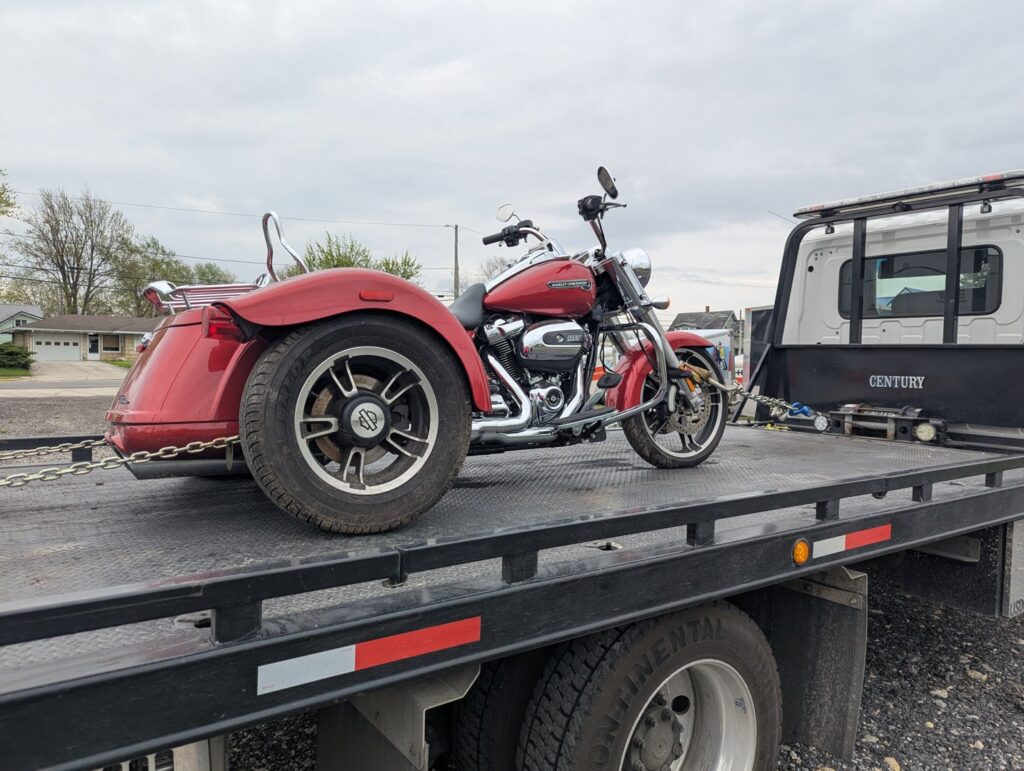 A red three-wheeled motorcycle being transported on a flatbed tow truck by First Hand Towing & Recovery in Fort Wayne, IN.