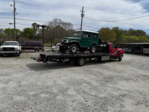 A red flatbed tow truck from Advance Towing & Recovery hauling a green SUV in Columbus, GA.