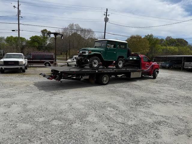 A red flatbed tow truck from Advance Towing & Recovery hauling a green SUV in Columbus, GA.