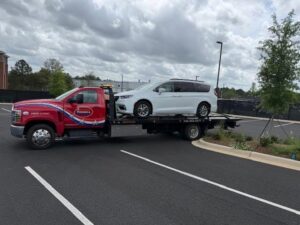 A red flatbed tow truck from Advance Towing & Recovery hauling a white minivan in Columbus, GA.