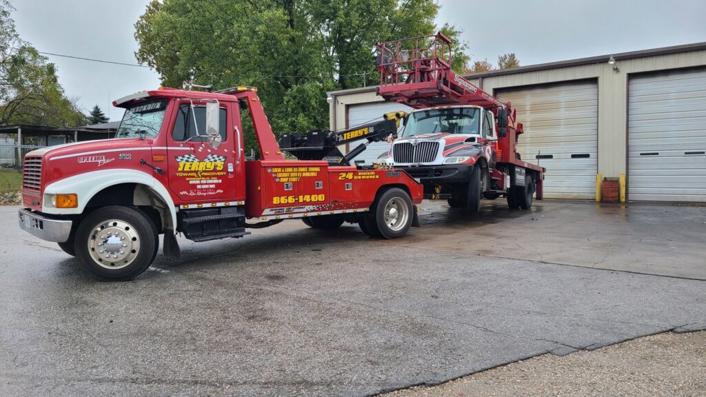 A red tow truck from Terry's Auto Service and Towing, LLC, towing a truck with a boom lift in Springfield, MO.