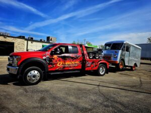A red Jensen Towing truck towing a blue and silver delivery van in Kenosha, WI.