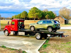 A red flatbed tow truck from Rubber Chicken Towing LLC towing a green SUV on its bed in Charlotte, NC.