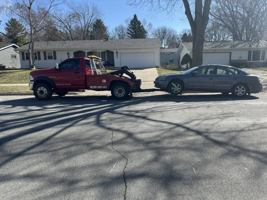 A red PNB towing truck transporting a grey sedan on a residential street in Madison, WI.
