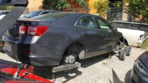 A red tow truck from Alanis Wrecker Service towing a grey sedan using dollies in San Antonio, TX.