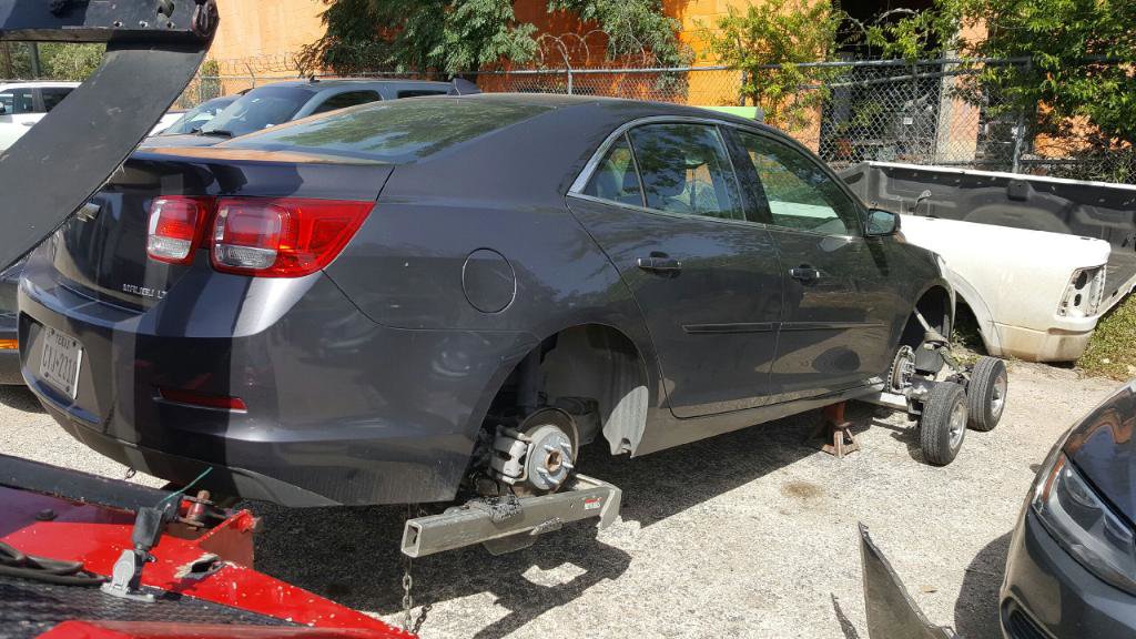 A red tow truck from Alanis Wrecker Service towing a grey sedan using dollies in San Antonio, TX.