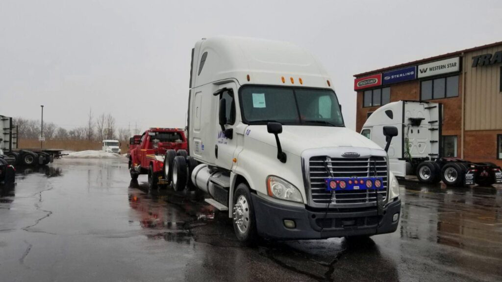 A red tow truck from Chicago Towing towing a semi-truck cab with a wheel lift in Chicago, IL.