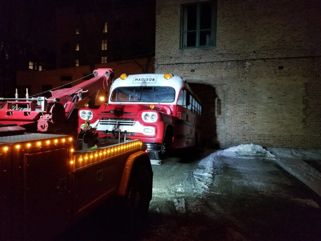 A red tow truck from Chicago Towing towing a vintage red and white bus in the dark in Chicago, IL.