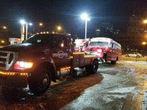A red tow truck from Chicago Towing towing a vintage red and white bus at night in Chicago, IL.