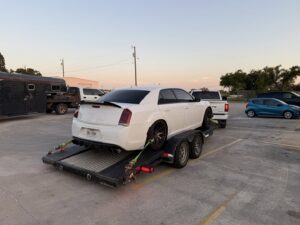 A red tow truck transporting a black car on its flatbed at night for RDZ Towing Service 24/7 in Dallas, TX.