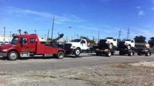A red Glenn's Towing & Recovery Inc tow truck transporting multiple white pickup trucks on a trailer in Lafayette, LA.