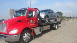 A red tow truck transporting a grey pickup truck on its flatbed for Vatos Locos Towing in Cincinnati, OH.