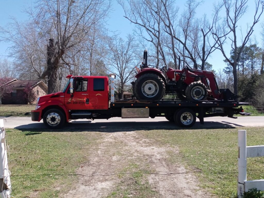 A red tractor loaded onto a flatbed tow truck from Full Circle Towing and Recovery in Dothan, AL.