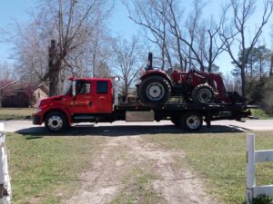 A red tractor loaded onto a flatbed tow truck from Full Circle Towing and Recovery in Dothan, AL.