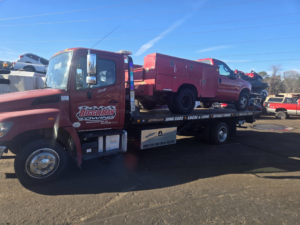 A red utility truck with toolboxes being transported on a flatbed tow truck by Riggleman Towing in Moorefield, WV.