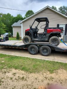 A red UTV secured on a flatbed trailer for transport from B'ham Trailer Rentals in Alabaster, AL.