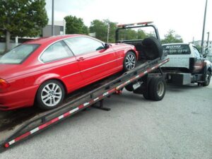 A red van being towed by a wheel-lift tow truck by Baltimore Towing Service LLC in Owings Mills, MD.