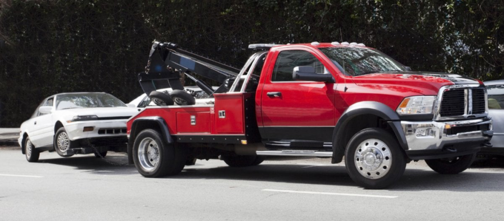 A red wrecker tow truck actively towing a white car for Towing Services Of Omaha in Omaha, NE.