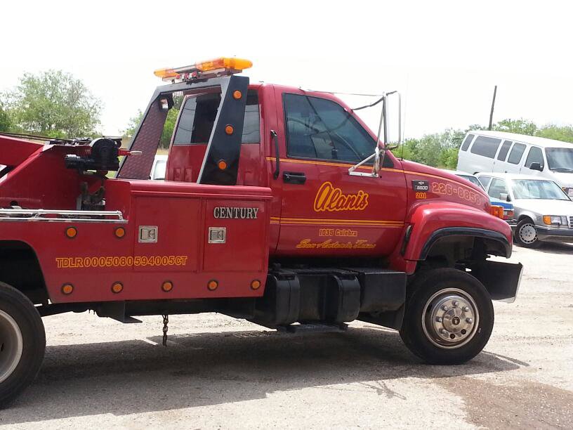Side view of a red wrecker truck with Alanis Wrecker Service branding parked in San Antonio, TX.