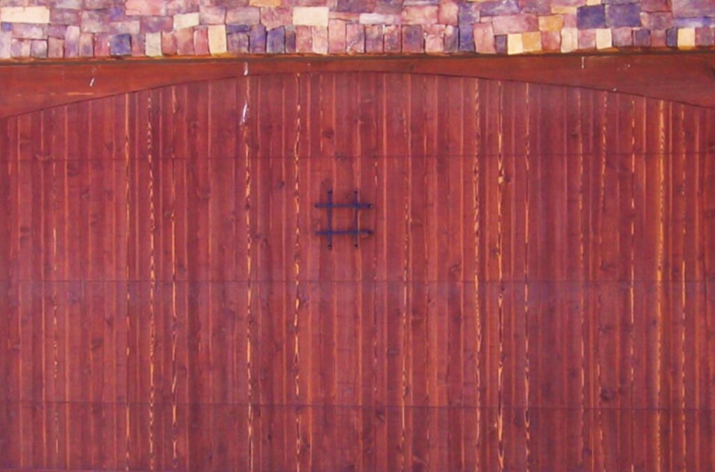 A reddish-brown wooden garage door with a decorative metal accent, installed by Mark's Garage Door Services in Santa Fe, NM.