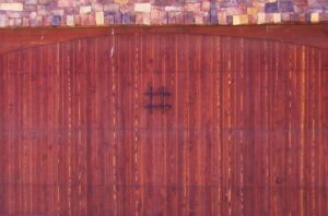 A reddish-brown wooden garage door with a decorative metal accent, installed by Mark's Garage Door Services in Santa Fe, NM.