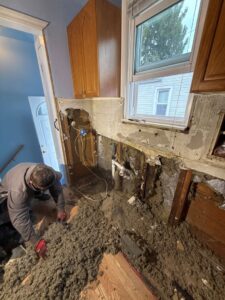 A water damage specialist removing wet insulation from a kitchen wall during a water damage restoration project by H2O Pros Water Restoration Services in Westland, MI.