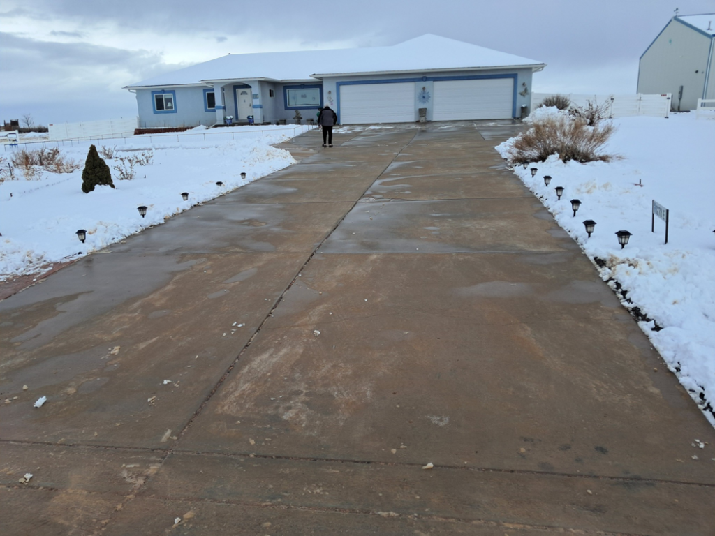 A residential concrete driveway cleared of snow, with snow piled neatly on the sides, showcasing snow removal by NO LEAKS Irrigation & Landscaping LLC in Pueblo, CO.