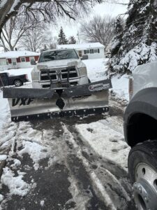 A snow plow truck clearing a residential driveway by Lovett lawn care & snow removal in Omaha, NE.