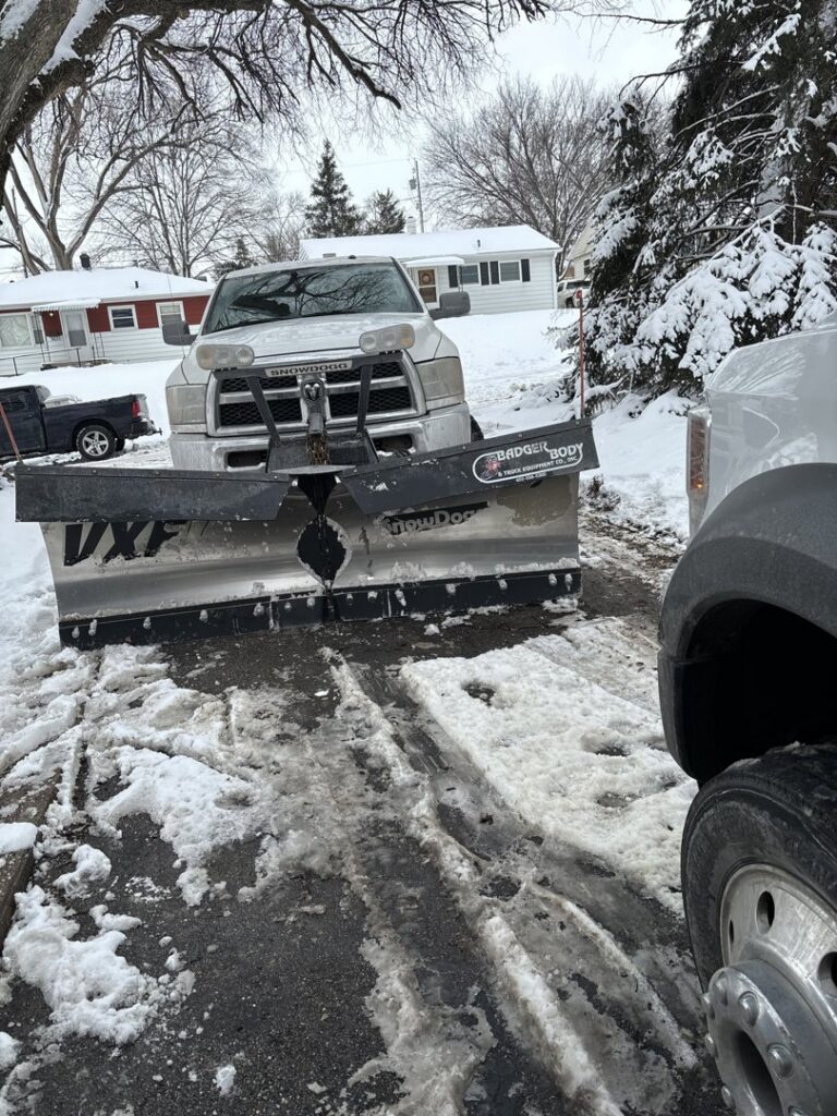 A snow plow truck clearing a residential driveway by Lovett lawn care & snow removal in Omaha, NE.