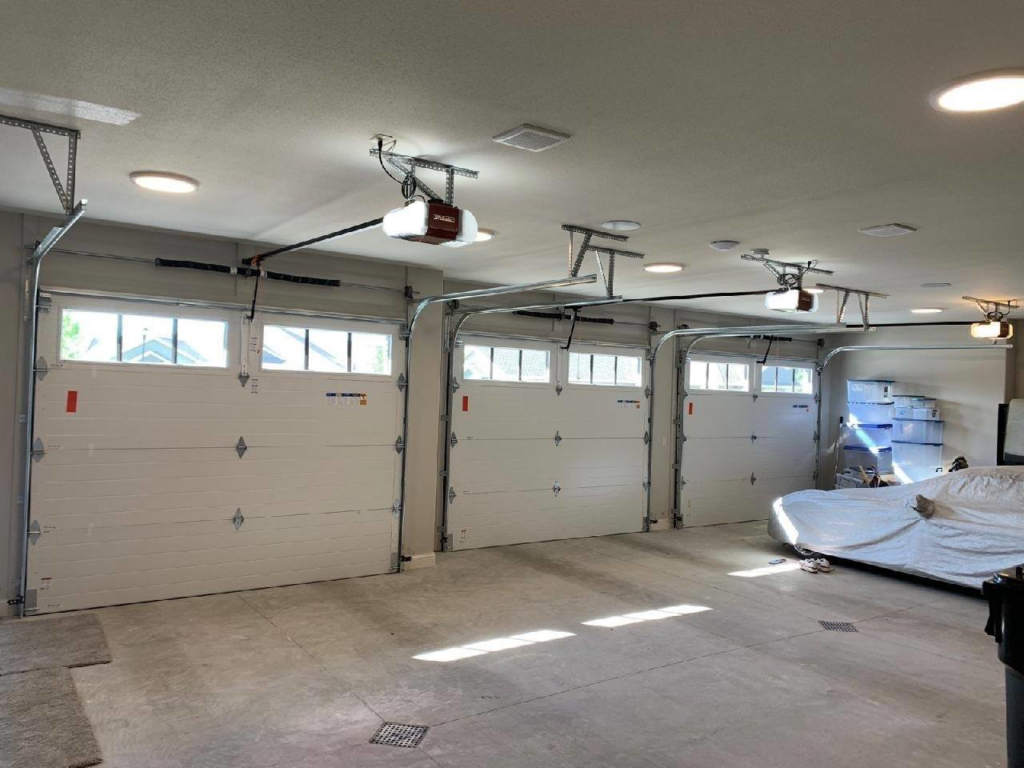 Interior view of a garage showing three newly installed white residential garage doors and openers by McCody Overhead Doors in Williston, ND