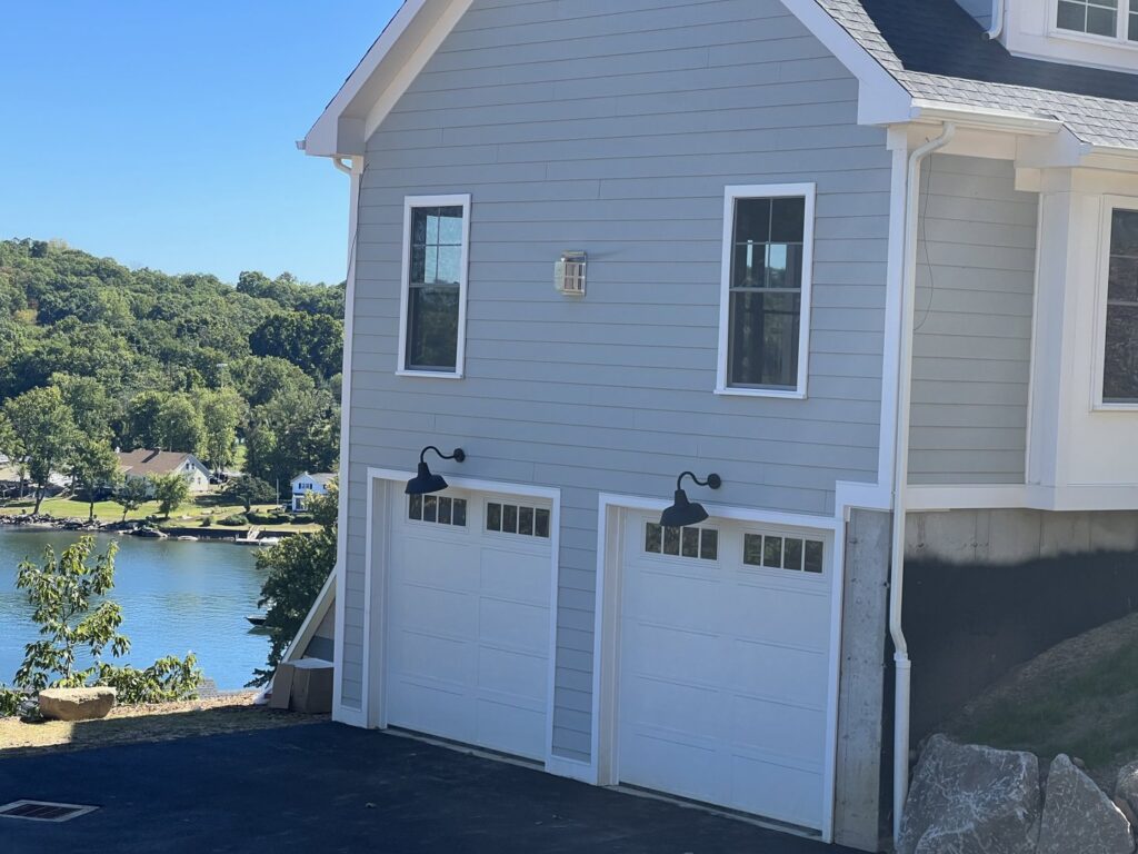 Two modern white garage doors on a residential home with a scenic lake view, installed by RidgeLine Overhead Garage Door of CT in Danbury, CT