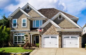 A beautiful residential house featuring two white garage doors with windows and decorative hardware by PS GARAGE DOORS in Grand Forks, ND