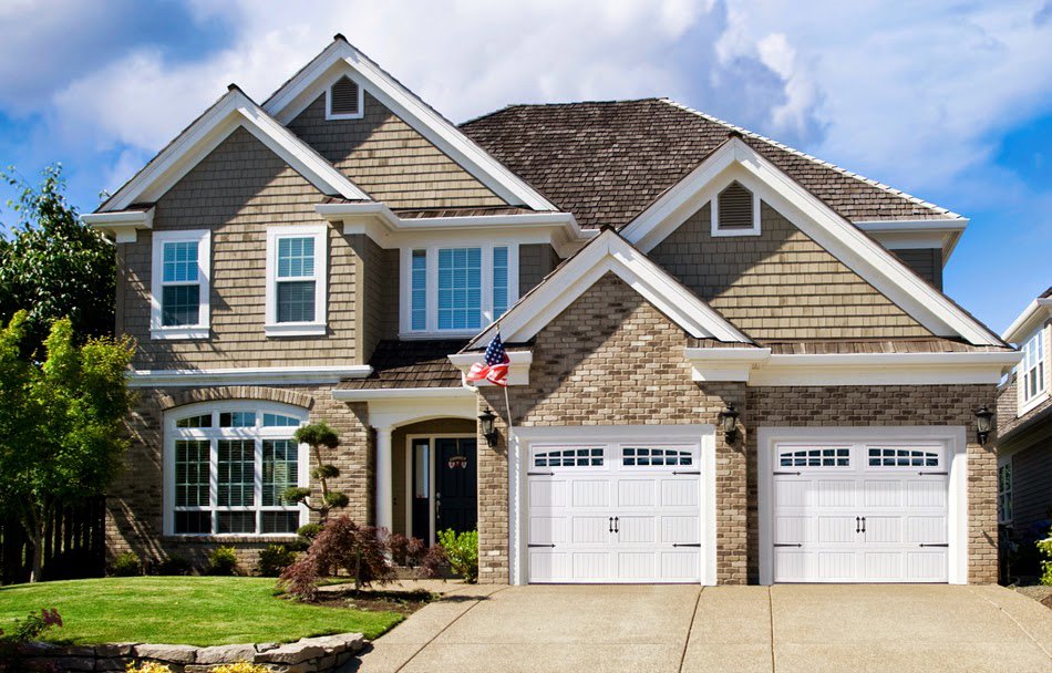 A beautiful residential house featuring two white garage doors with windows and decorative hardware by PS GARAGE DOORS in Grand Forks, ND