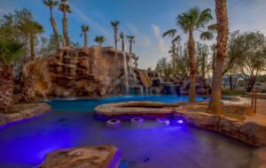 An elaborate resort-style pool featuring rock waterfalls, slides, and vibrant blue lighting by Fix A Pool in Las Vegas, NV