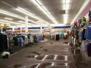 A retail store aisle with extensive standing water on the floor, indicating severe water damage in Oakland, CA by One Call Services of Oakland.