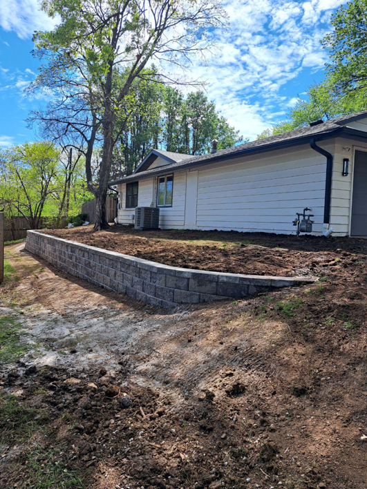A newly installed retaining wall next to a house by Arrow Foundation Repair in Shawnee, KS, preventing water damage.