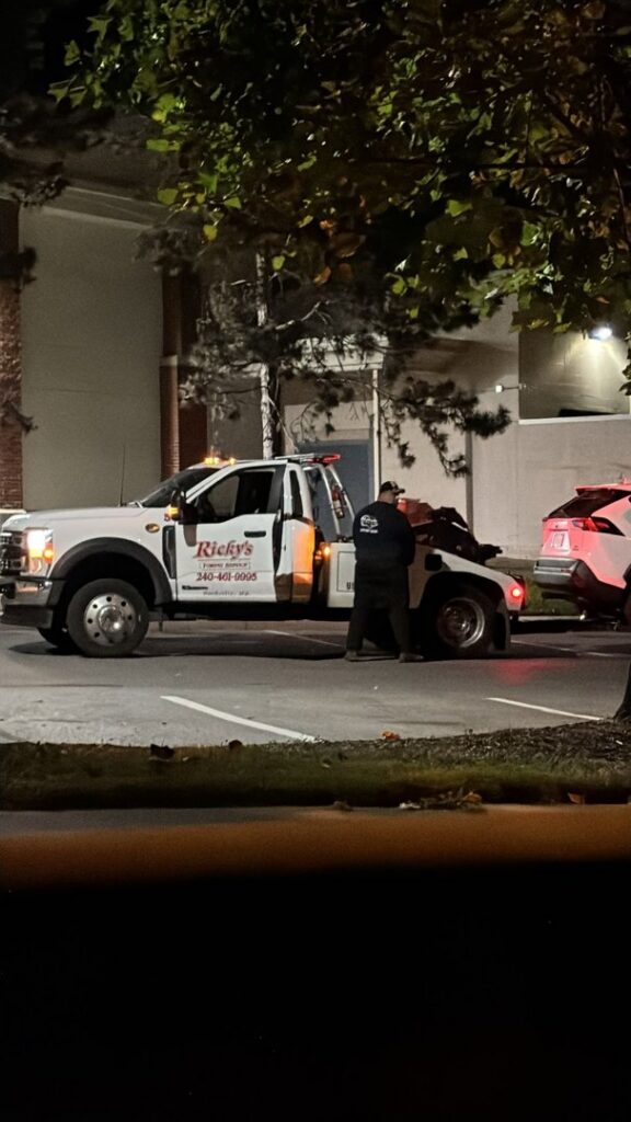 A Ricky's Towing & Recovery LLC tow truck with an operator working to secure a car for towing at night in Derwood, MD.