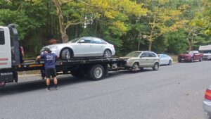 A Ricky's Towing & Recovery LLC flatbed tow truck transporting a silver car and towing a beige SUV with a wheel lift, providing comprehensive service in Derwood, MD.