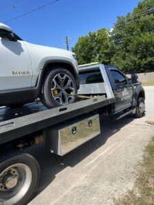 A white Rivian electric pickup truck being transported on a Jay Towing Services flatbed truck in Houston, TX.