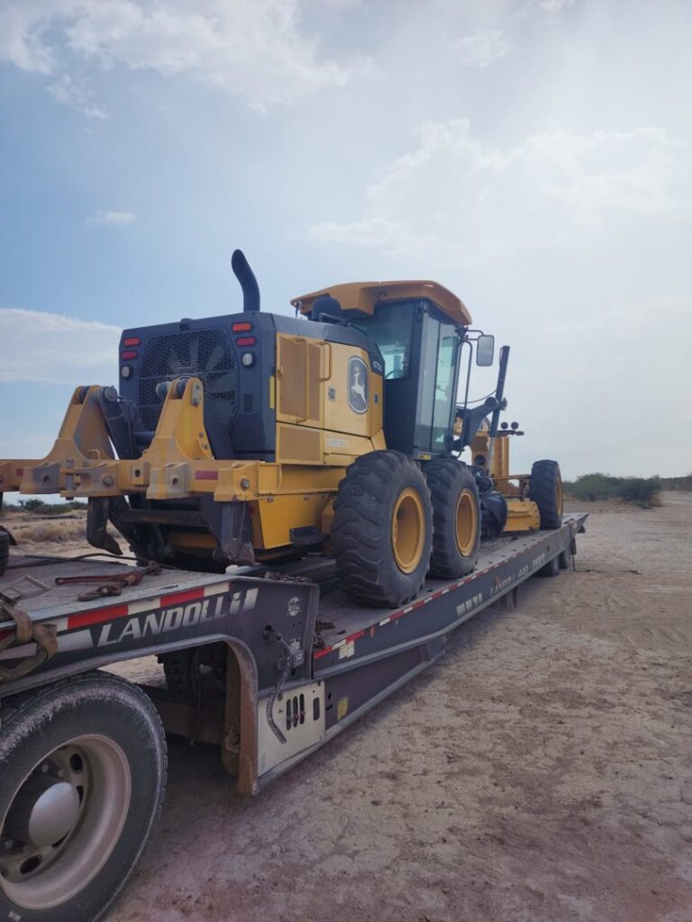 A large yellow road grader being transported on a heavy-haul flatbed trailer by CC Wrecker Service in Corpus Christi, TX.