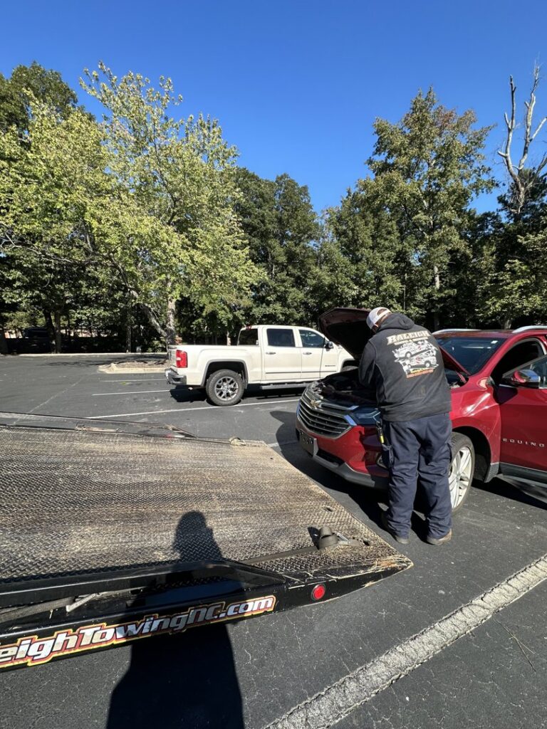 A Raleigh Towing & Recovery technician providing roadside assistance to a red SUV in Raleigh, NC.