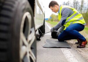 A service technician in a high-visibility vest changing a flat tire on the side of the road, a service provided by Emergency Towing Sacramento, CA.