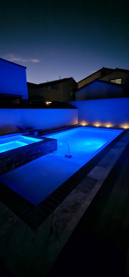 A robotic pool cleaner operating in a beautifully lit blue pool at night by AquaMac Pool Cleaning Service LLC in Reno, NV.
