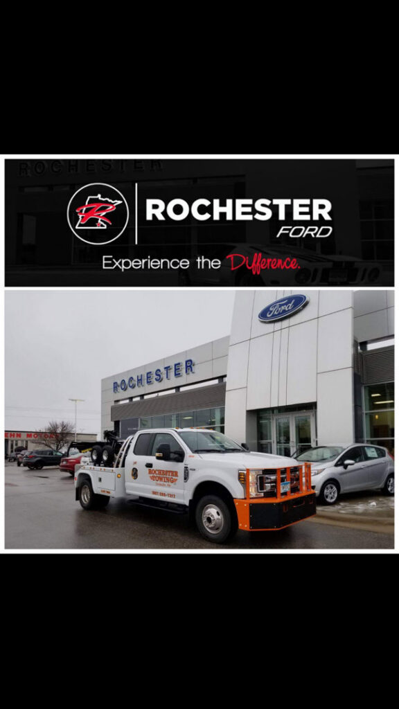 A white Rochester Towing truck parked in front of a Rochester Ford dealership in Rochester, MN.