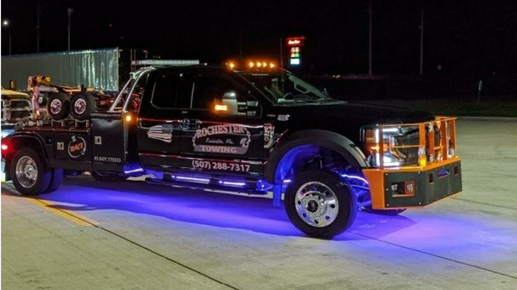 A black Rochester Towing truck with blue underglow lights parked at night, ready for service in Rochester, MN.