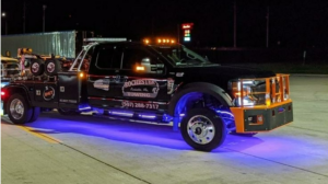 A black Rochester Towing truck with blue underglow lights parked at night, ready for service in Rochester, MN.