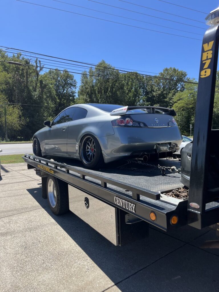 A black rollback tow truck from Tally's Towing and Recovery transporting a silver Nissan coupe in Owensboro, KY.