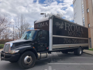 A Roma Moving truck parked in a commercial parking lot under a cloudy sky in Charlotte, NC.
